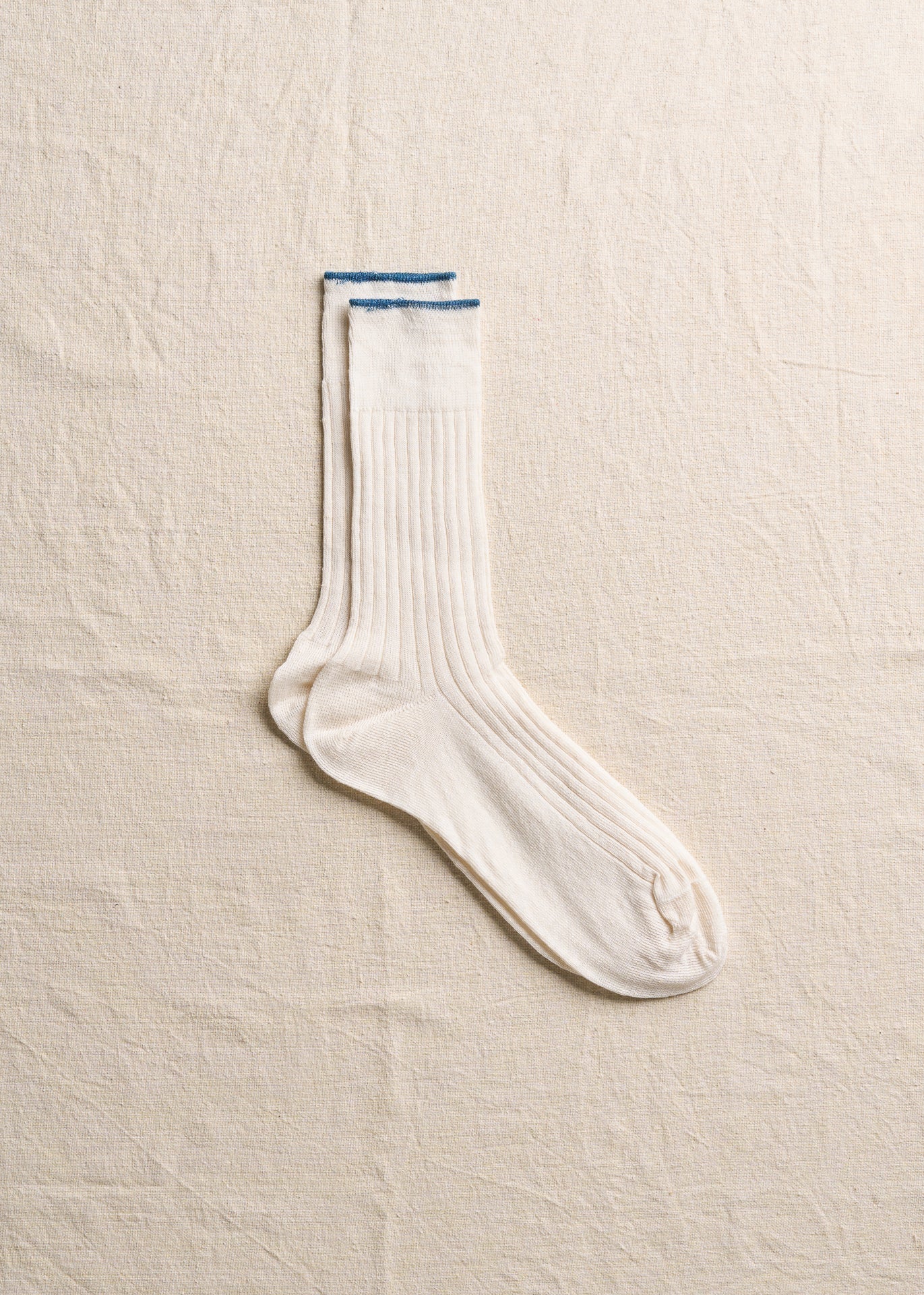 White linen ribbed men's socks laid flat on a neutral textured background.