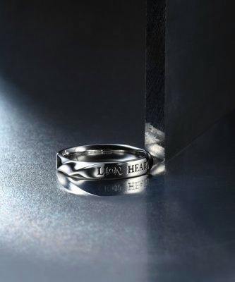 Silver duo ring engraved with "LION HEART" shown on a reflective surface beside a vertical block.