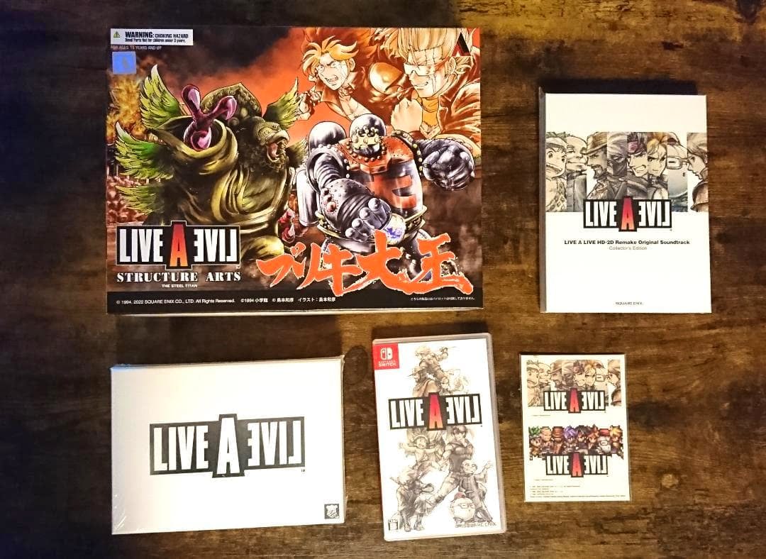 LIVE A LIVE collector's edition items for Nintendo Switch arranged on a wooden surface, including a large art board, boxed items, the Switch game case, and a small booklet.