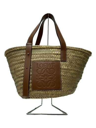 Beige LOEWE straw basket bag with brown leather handles and an embossed leather logo patch shown on a display stand.