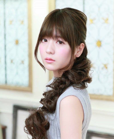 A model wearing a long S‑curl rope-style synthetic wig with bangs, shown from the side.