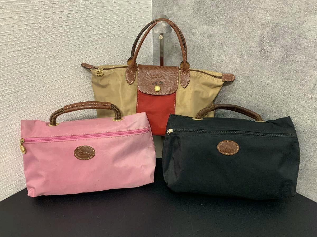 Three Longchamp nylon bags arranged on a table: a tan/red foldable tote at the back and pink and black handle-top pouches in front.