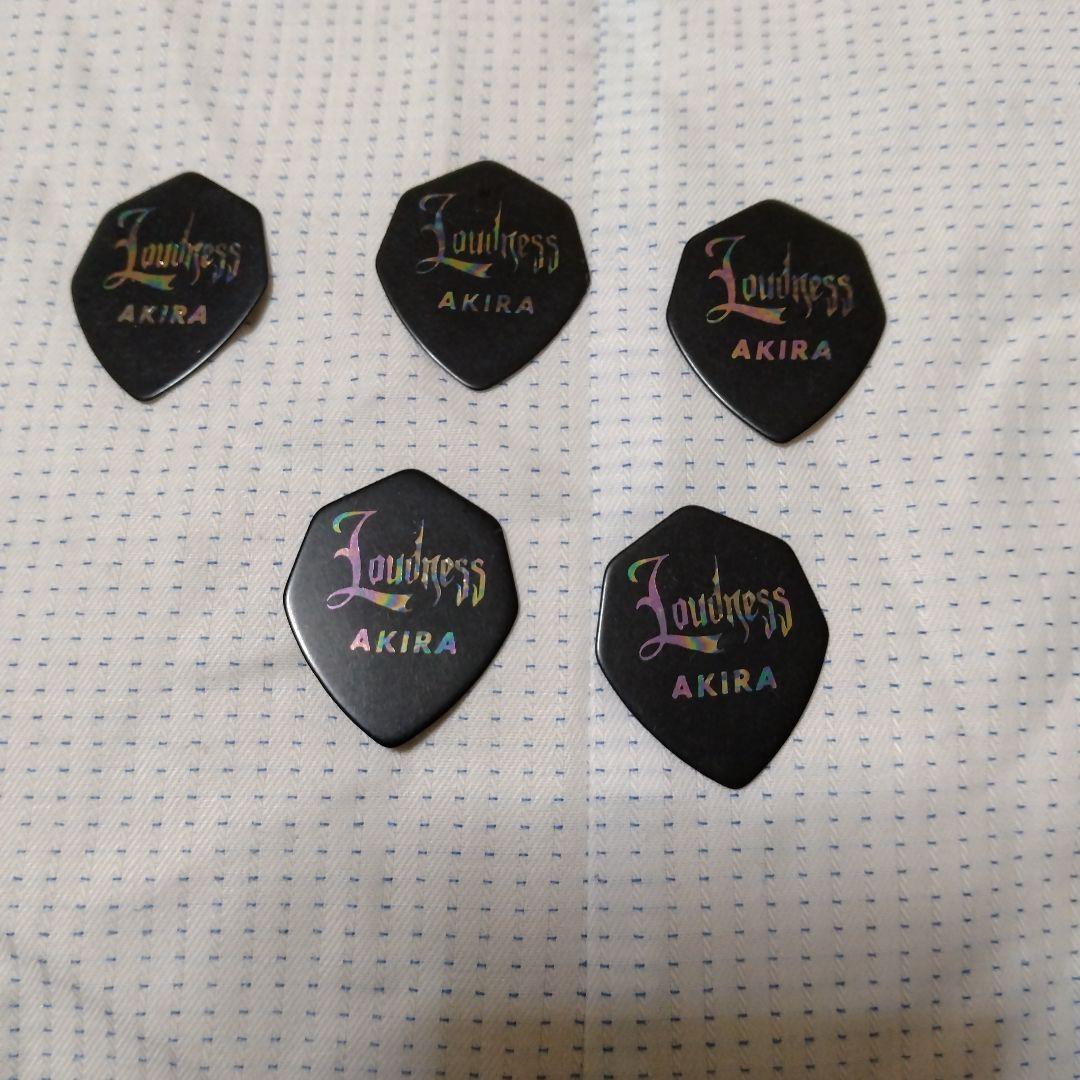 Five black guitar picks printed with "Loudness AKIRA" arranged on fabric.