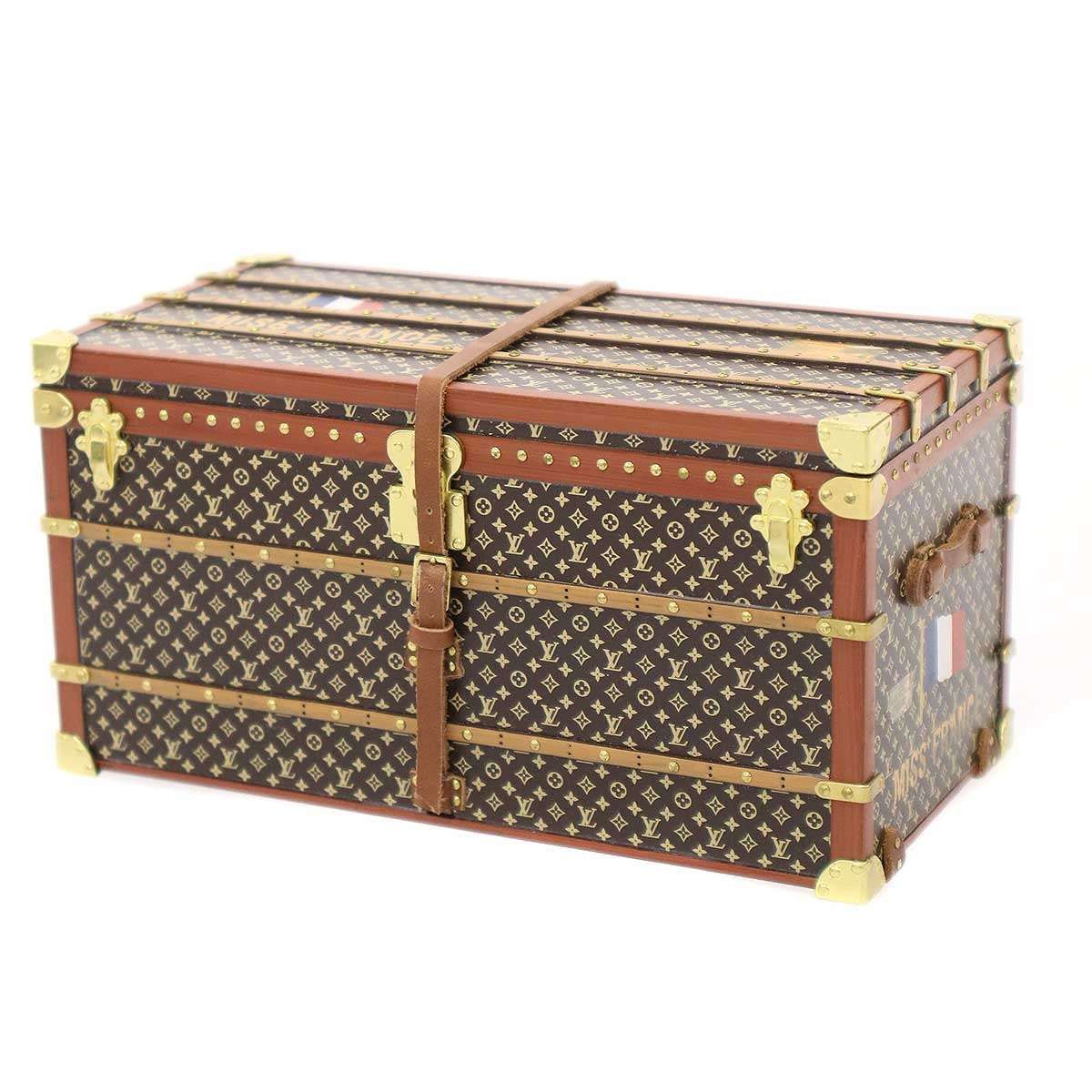 Louis Vuitton monogram trunk-shaped paperweight with leather strap and brass corner hardware on a white background.
