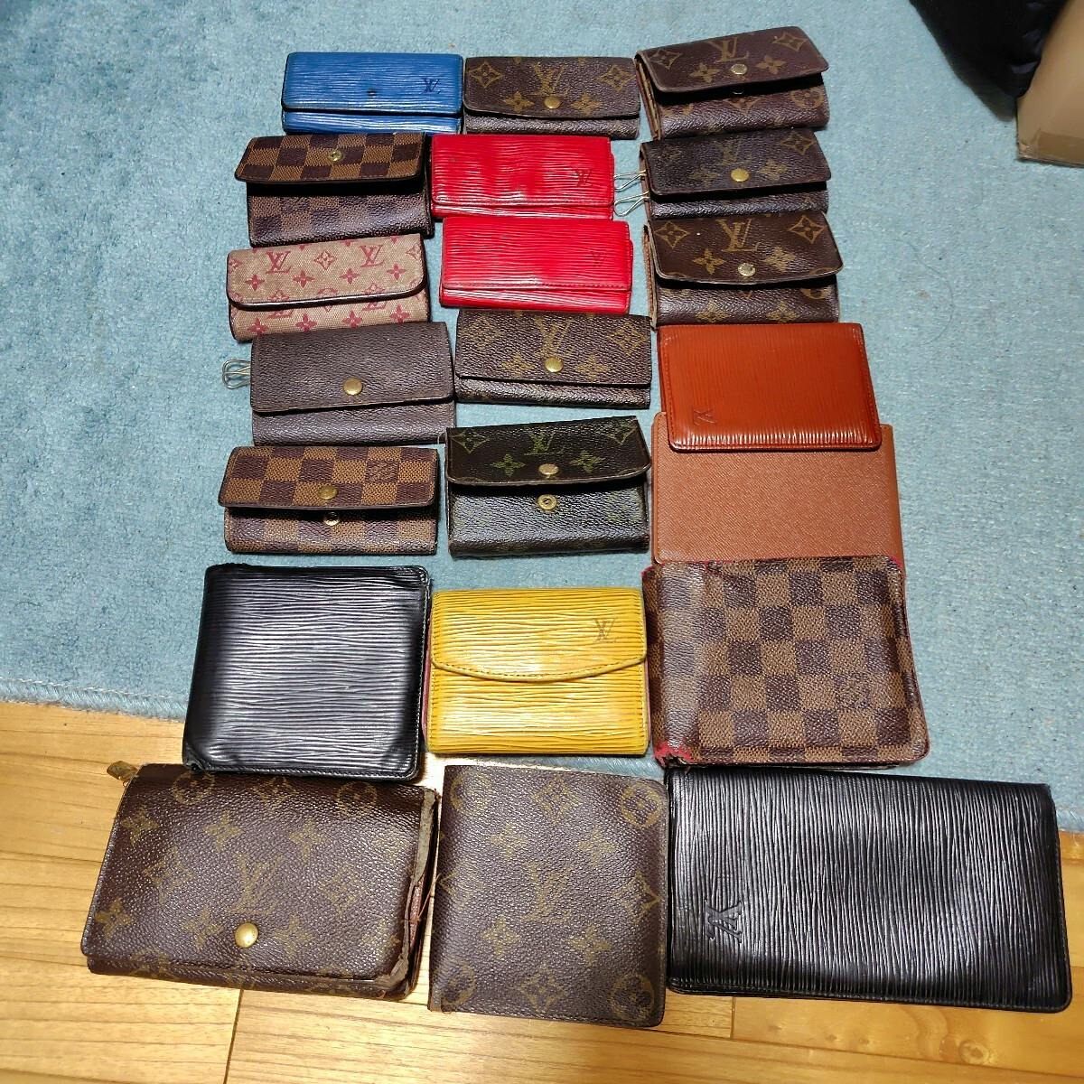 A laid-out assortment of Louis Vuitton wallets, key cases, and small pouches in monogram, Damier, and Epi leathers on a rug and wooden floor.