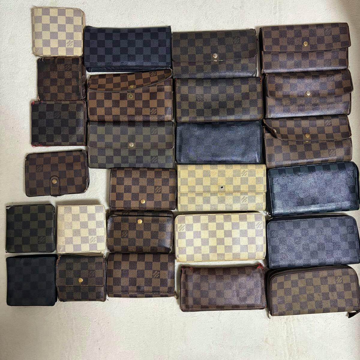 Top-down photo of a bulk set of Louis Vuitton wallets and small canvas wallets in Damier checkerboard patterns arranged in rows on a light surface.