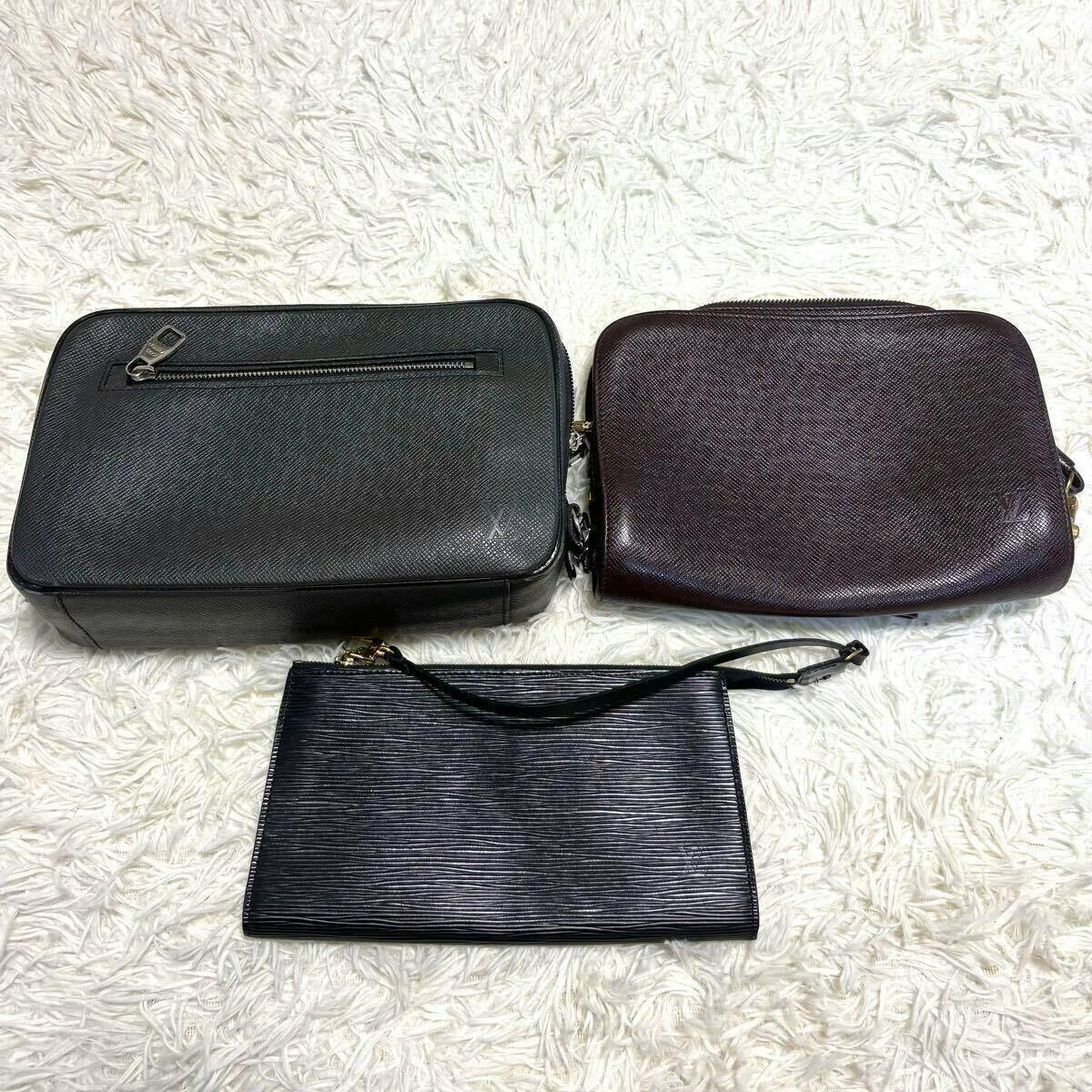 Three Louis Vuitton leather pouches laid flat on a white shag rug: two zip clutches and one slim wristlet.
