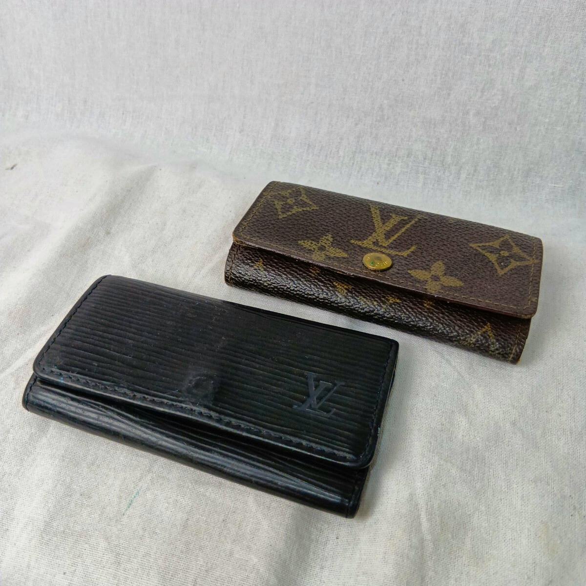 Two Louis Vuitton key cases, one monogram canvas and one black Epi leather, shown on a light fabric surface.