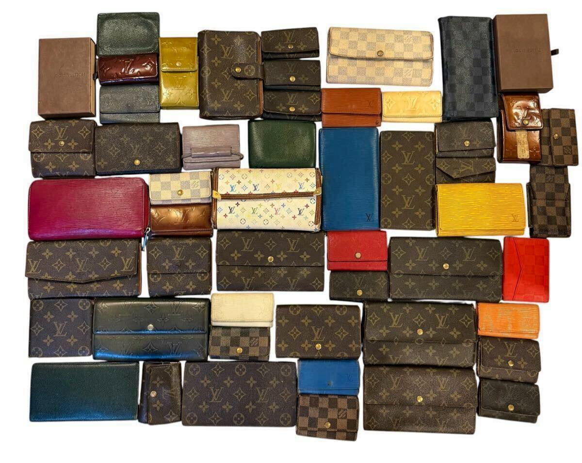 A flat lay of many Louis Vuitton wallets and small leather goods in various monogram, Damier, and Epi patterns arranged on a white background.