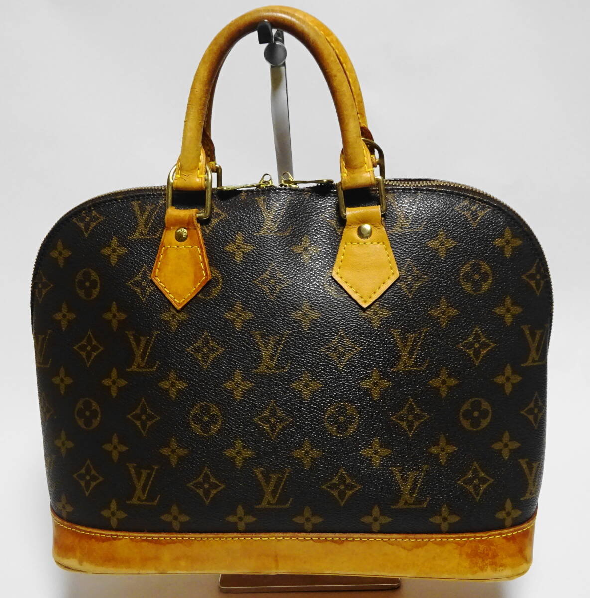 Front view of the Louis Vuitton Monogram Alma handbag showing vachetta leather handles and base with visible patina and wear.