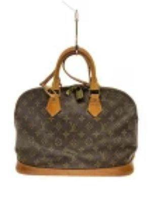 Front view of a Louis Vuitton Alma monogram canvas bag with leather handles and trim hanging from a hook.