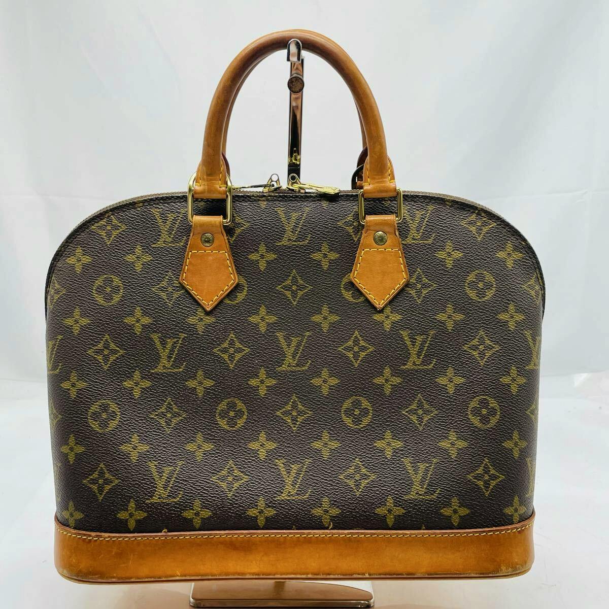Front view of a Louis Vuitton Alma PM monogram handbag with leather trim and two top handles.
