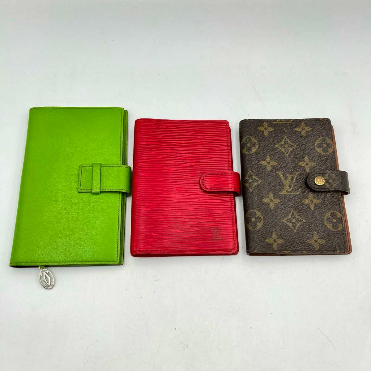 Three leather notebook covers/wallets displayed side by side: green, red, and brown monogram.