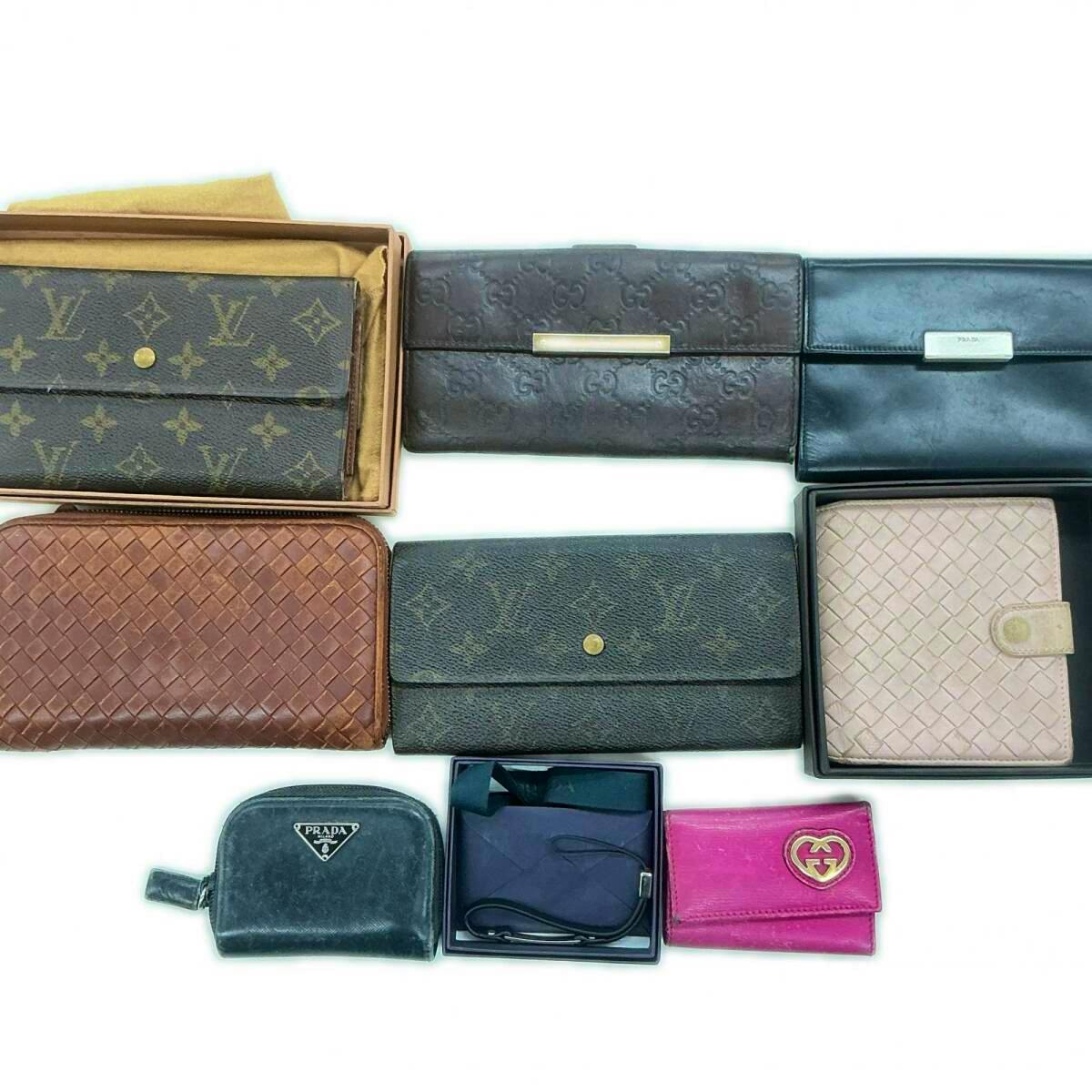 Top-down photo of nine assorted branded wallets and small leather goods, including a Louis Vuitton monogram wallet, arranged on a white background.
