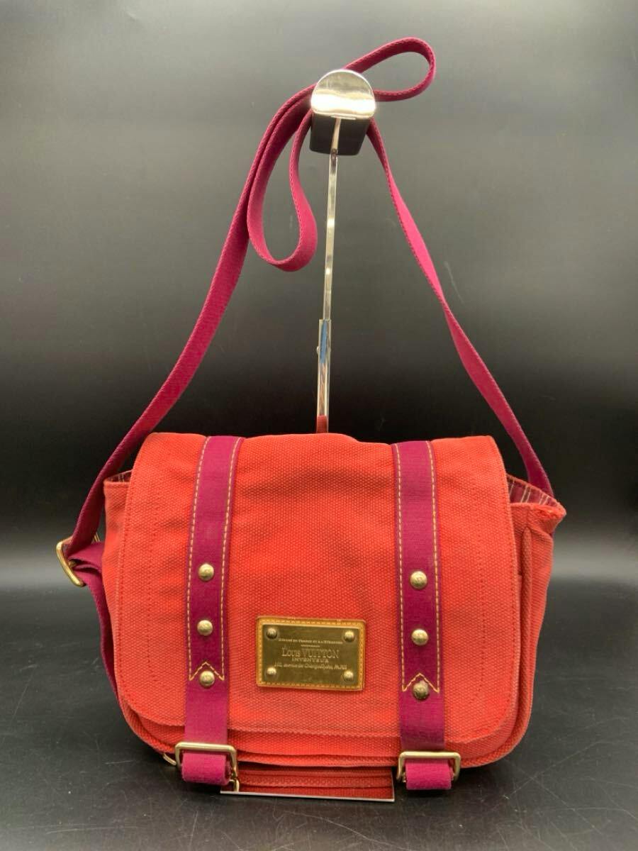 Front view of a red Louis Vuitton shoulder bag with contrasting pink straps and a brass Louis Vuitton name plate.