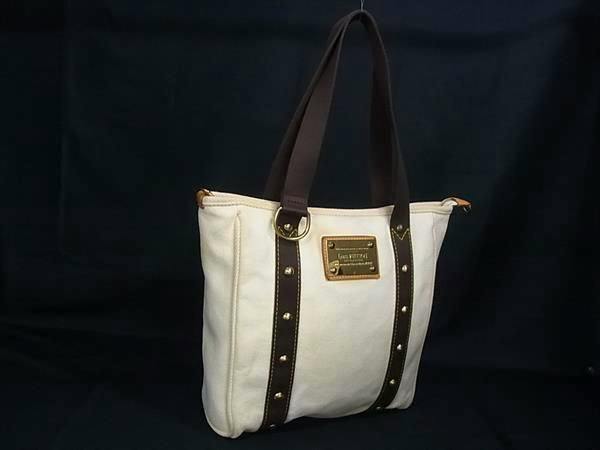 Ivory Louis Vuitton Antigua Cabas MM tote bag with brown straps and a gold-tone plaque against a dark background.