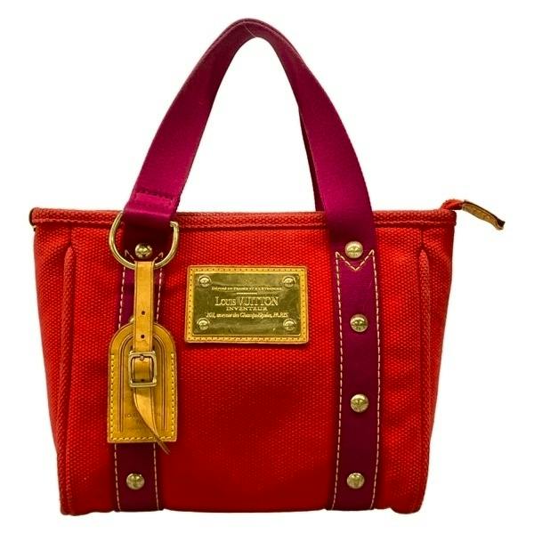 Front view of a red Louis Vuitton canvas tote bag with purple handles and a gold logo plate.
