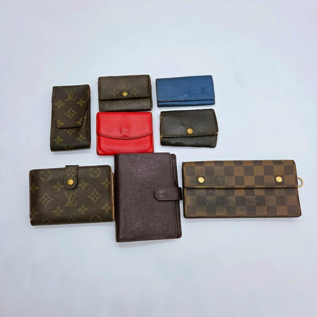 Several Louis Vuitton wallets and small leather accessories in monogram, checkered, and colored leathers arranged on a white background.