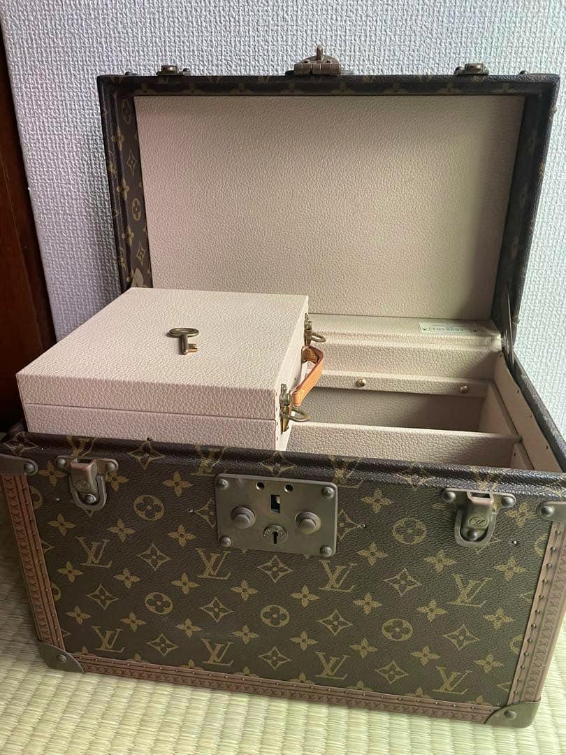 Open Louis Vuitton monogram trunk showing the beige interior, a small removable box, and a key inside.