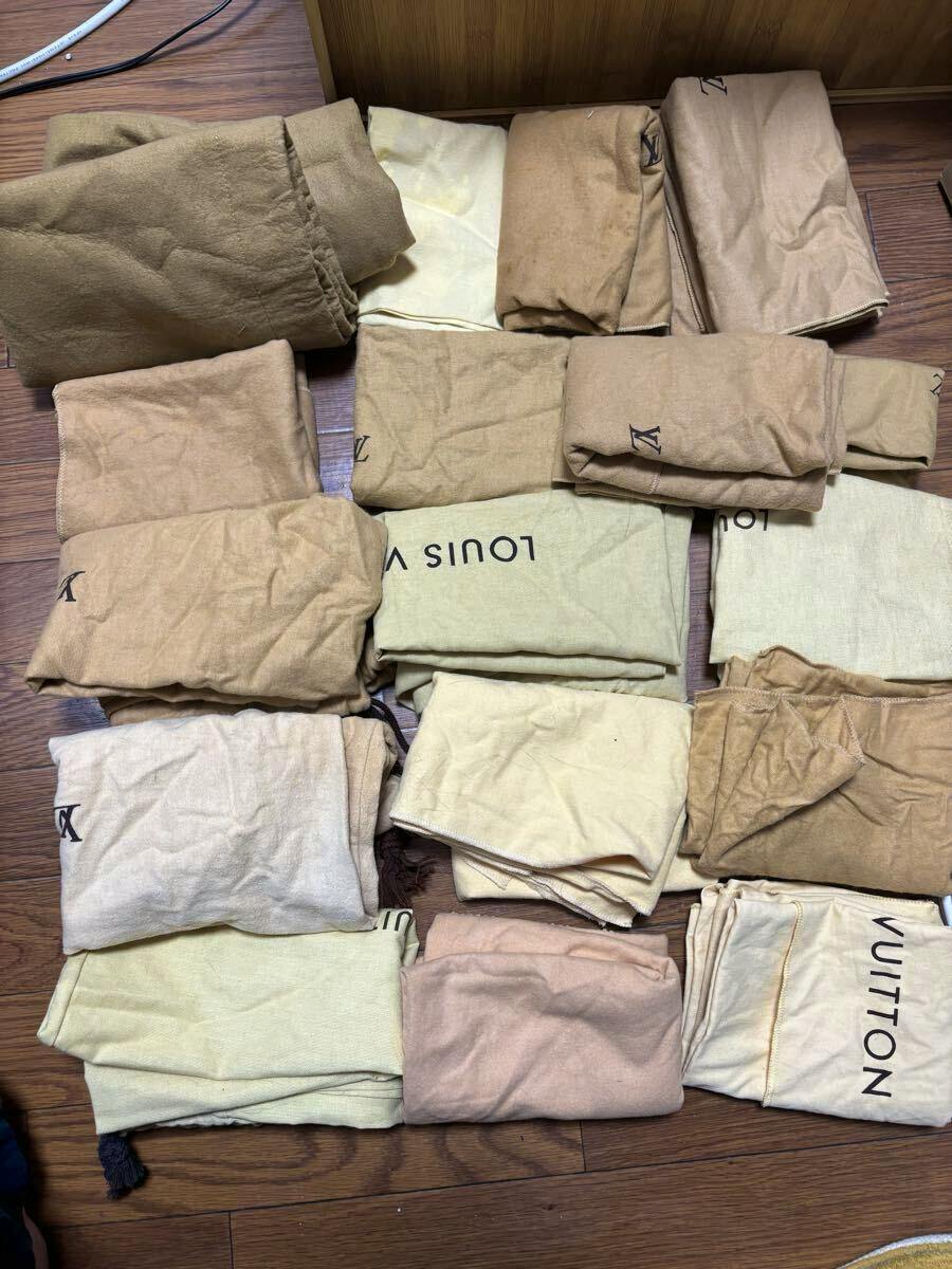 Multiple folded Louis Vuitton branded cloth dust bags in various tan and cream shades laid out on a wooden floor.