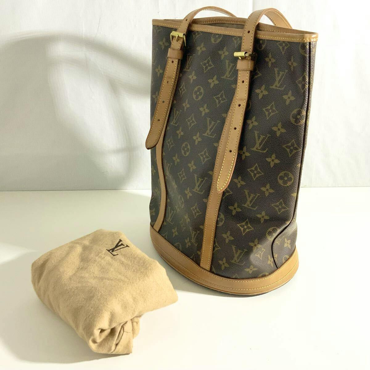 Brown Louis Vuitton monogram Bucket GM tote bag with leather trim shown standing next to a folded dust pouch.