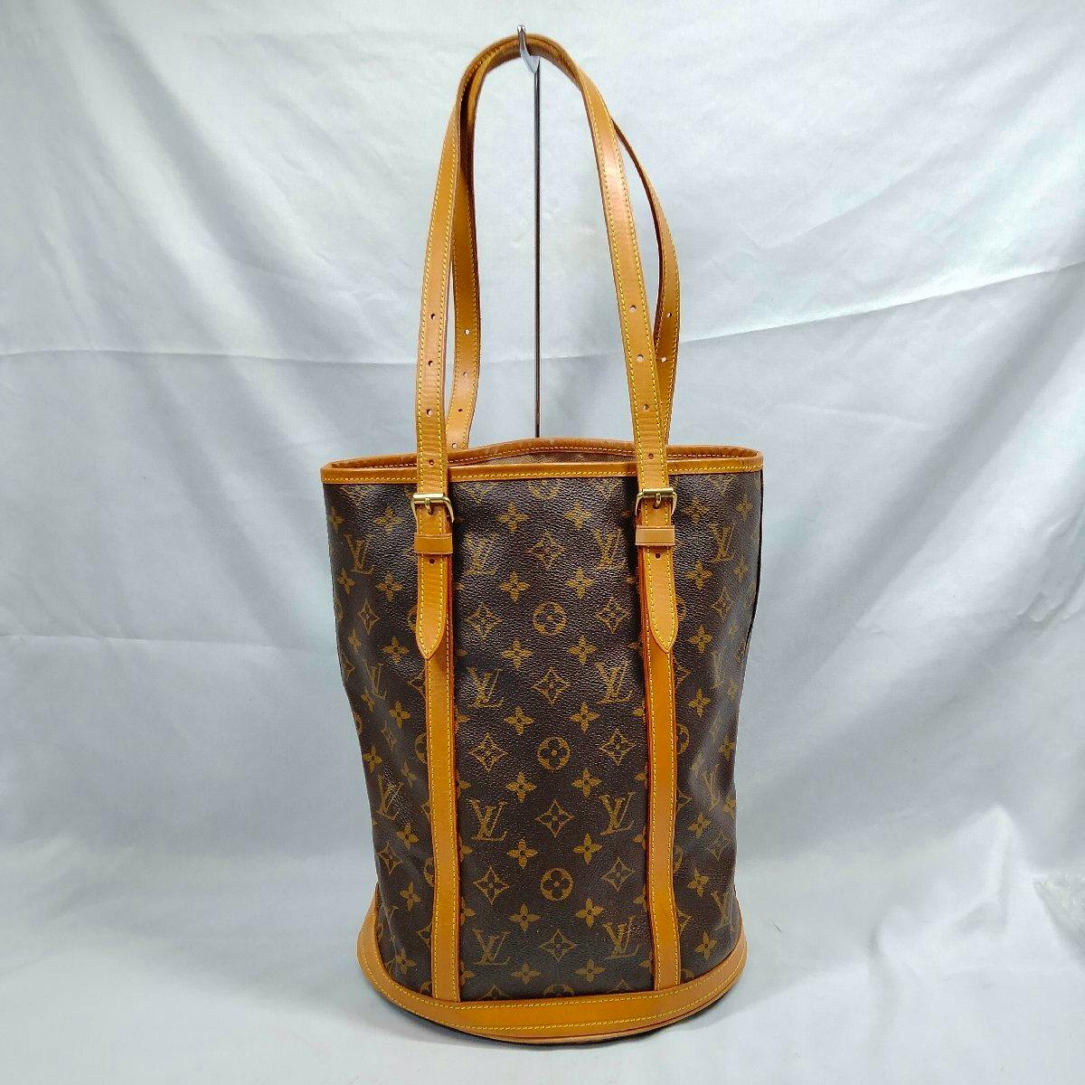 Front view of a Louis Vuitton Monogram Bucket GM bag showing the monogram canvas with tan leather trim and shoulder straps on a plain backdrop.
