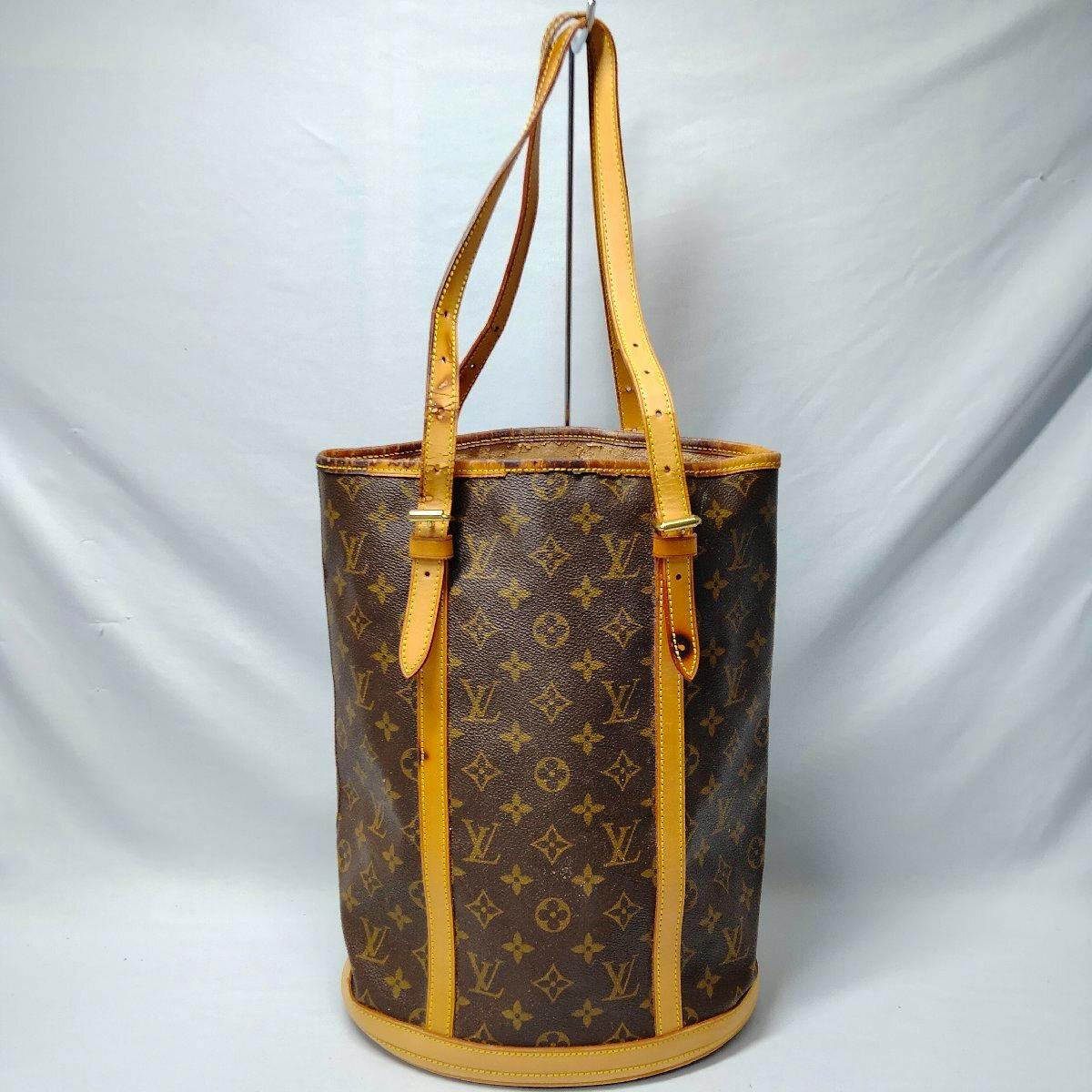 A Louis Vuitton Bucket GM monogram shoulder bag standing upright with two leather shoulder straps and trim.