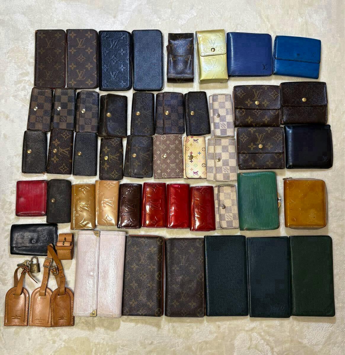 Many Louis Vuitton wallets, key cases, and small leather goods arranged in rows on a light surface.