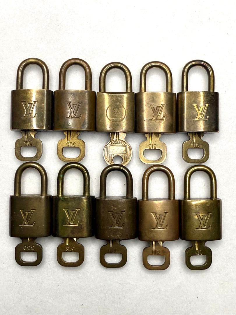 Ten brass Louis Vuitton padlocks with keys arranged in two rows on a white background.
