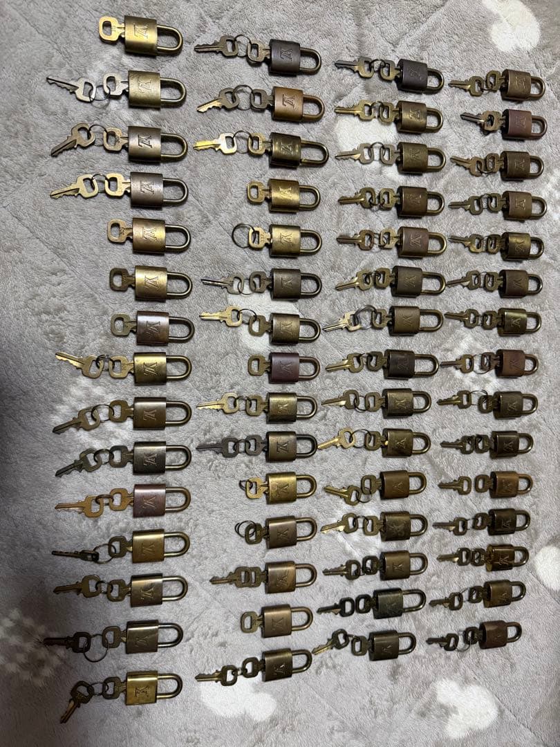 Many Louis Vuitton padlocks with their keys arranged in rows on a fabric surface.
