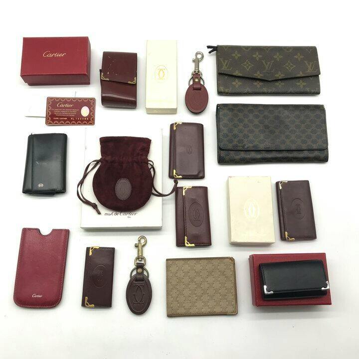 Multiple small wallets, key cases, pouches, and boxes arranged on a white background, including Louis Vuitton and Cartier items.