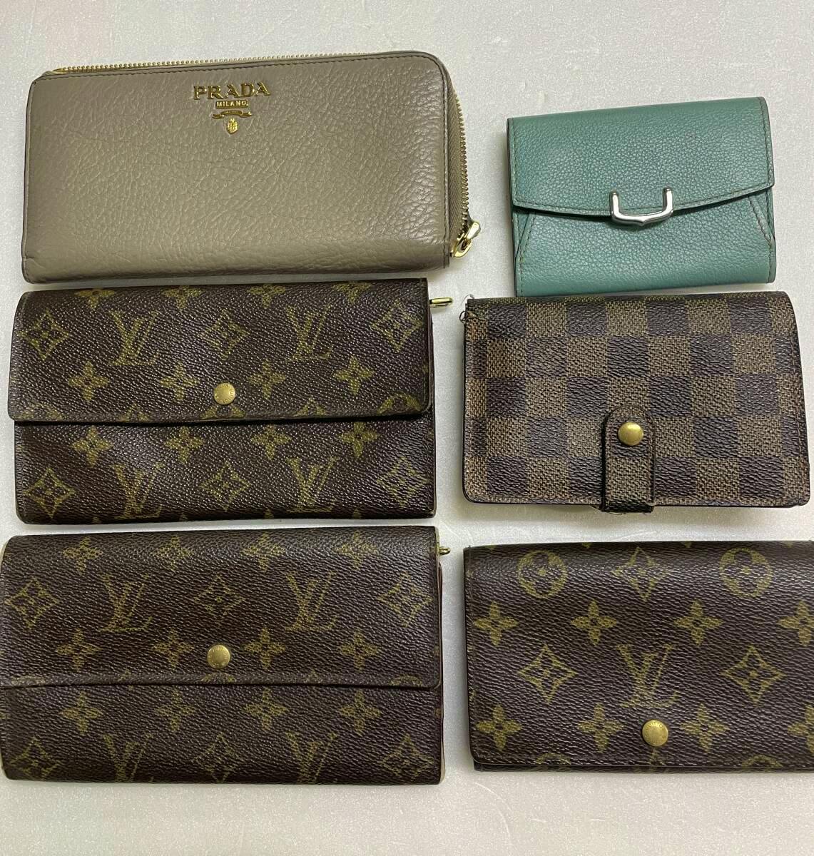 Six used wallets and card holders laid flat, including multiple Louis Vuitton monogram pieces and a Prada zip wallet.
