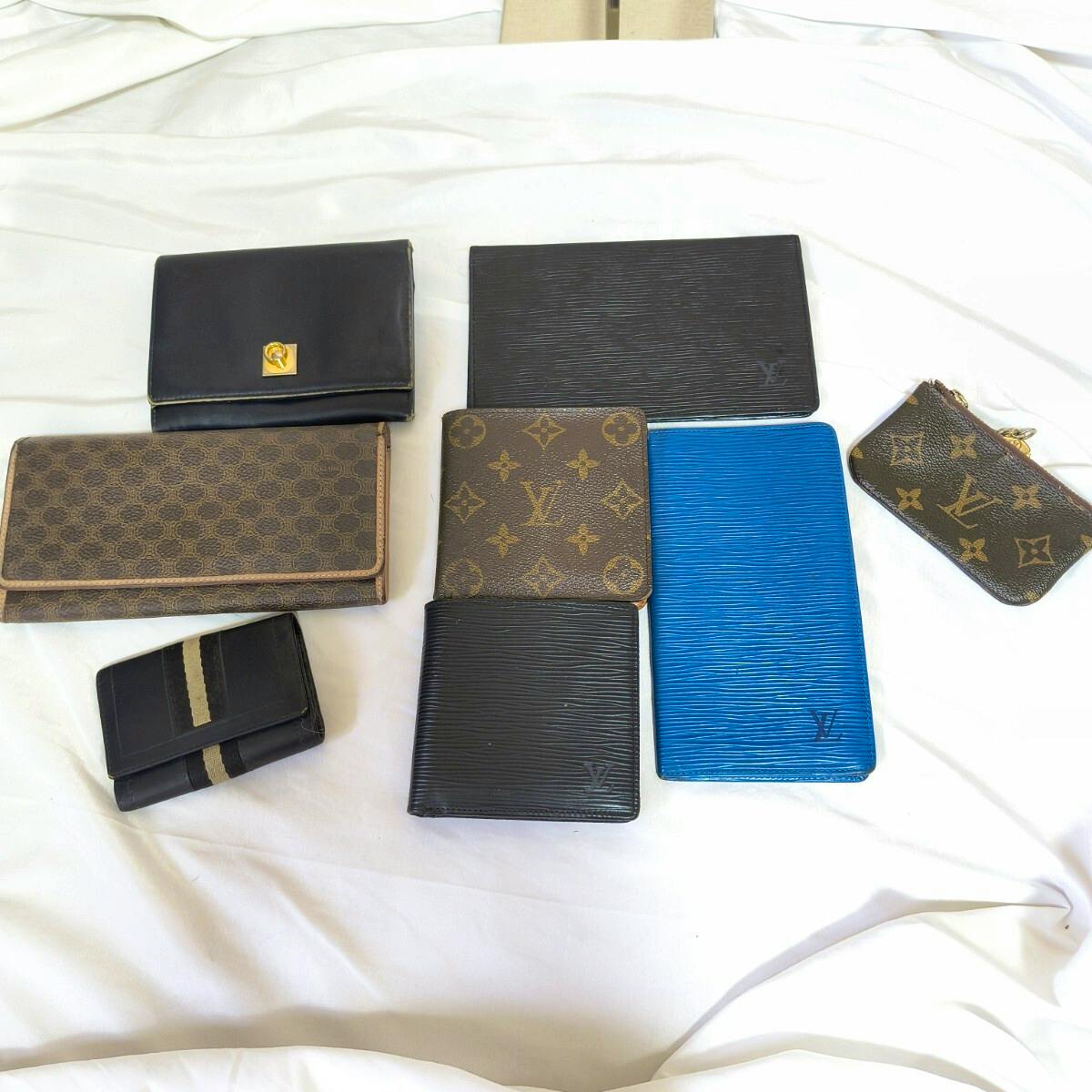 Eight branded wallets and small leather goods, including Louis Vuitton monogram pieces, arranged on a white sheet.
