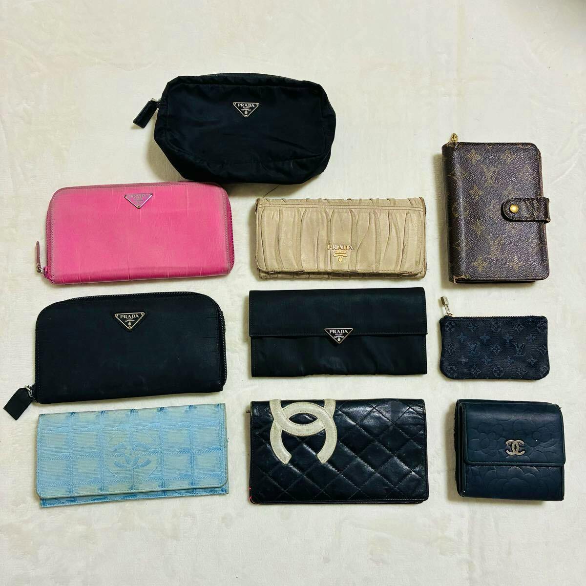Flat lay of multiple wallets and small leather goods (Prada, Louis Vuitton, Chanel) arranged on a light background.