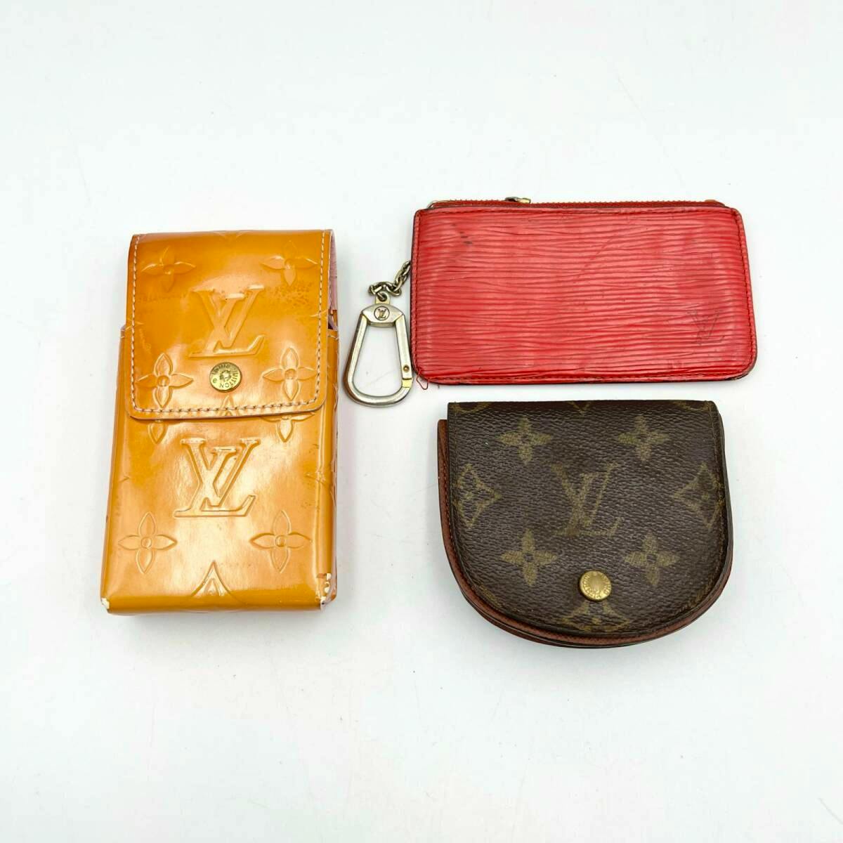Three Louis Vuitton items — a cigarette case, a red zip coin pouch with key hook, and a monogram coin case — arranged on a white background.