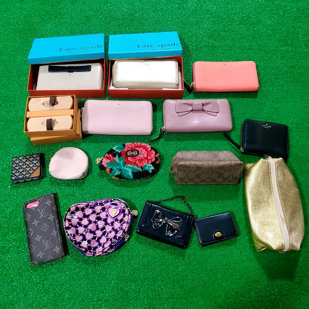 Multiple branded wallets, pouches, and small accessories arranged on a green surface as a mixed lot.