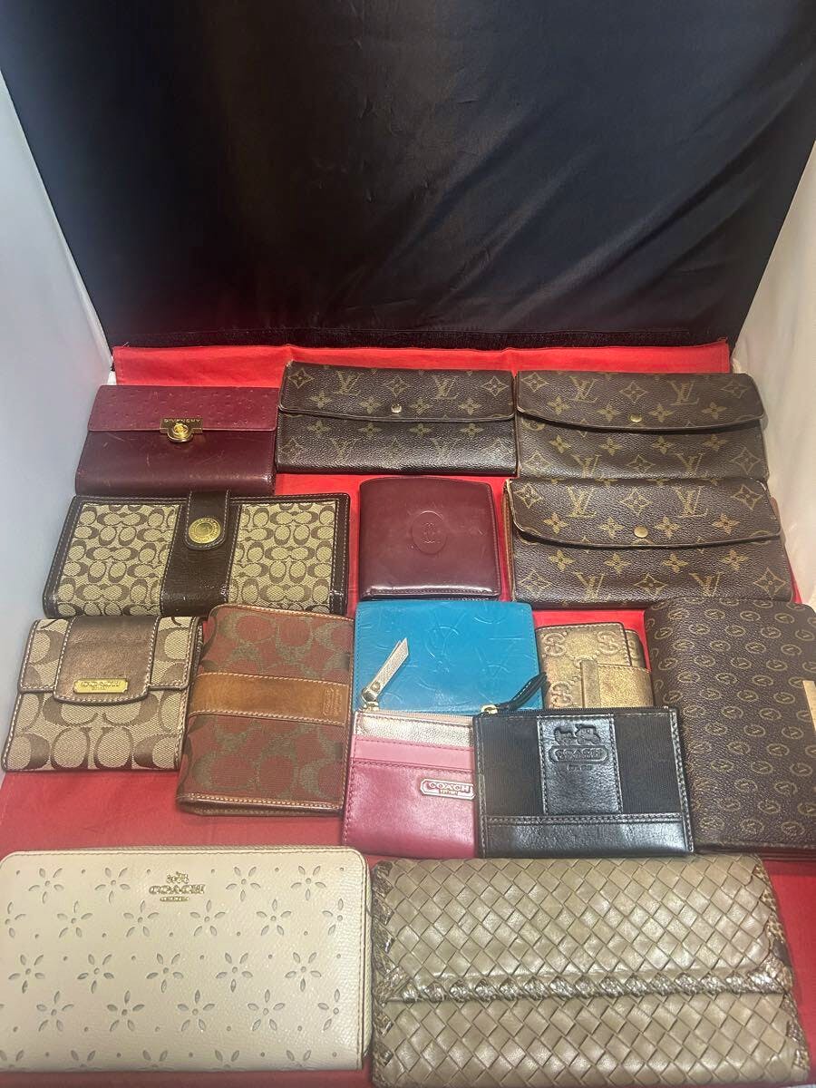 Assorted wallets, coin purses, and key cases (including several Louis Vuitton monogram pieces) arranged on a red cloth background.