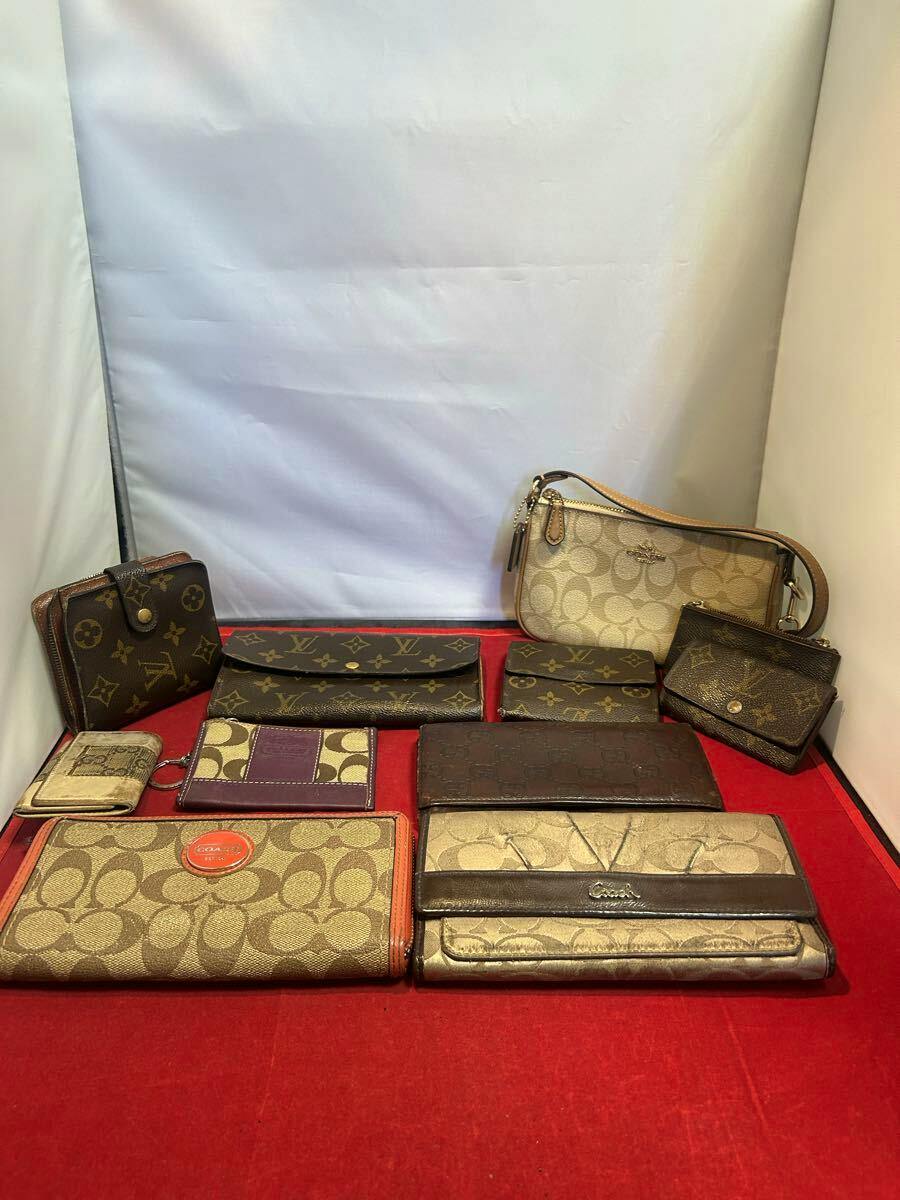 Multiple wallets, key cases, and coin cases from brands including Coach, Louis Vuitton, and Gucci displayed on a red surface against a white background.