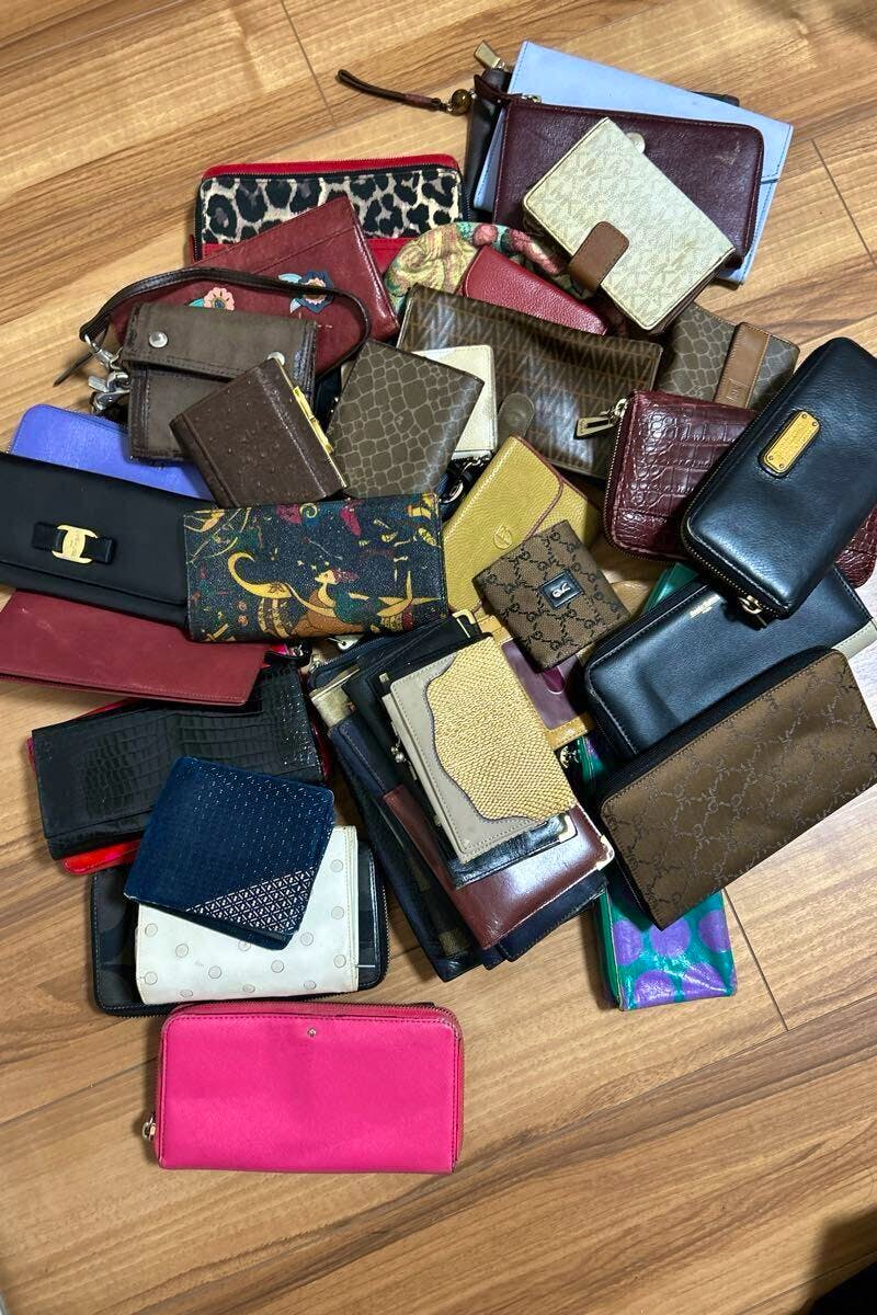 Top-down photo of many assorted branded wallets and small leather accessories spread on a wooden floor.
