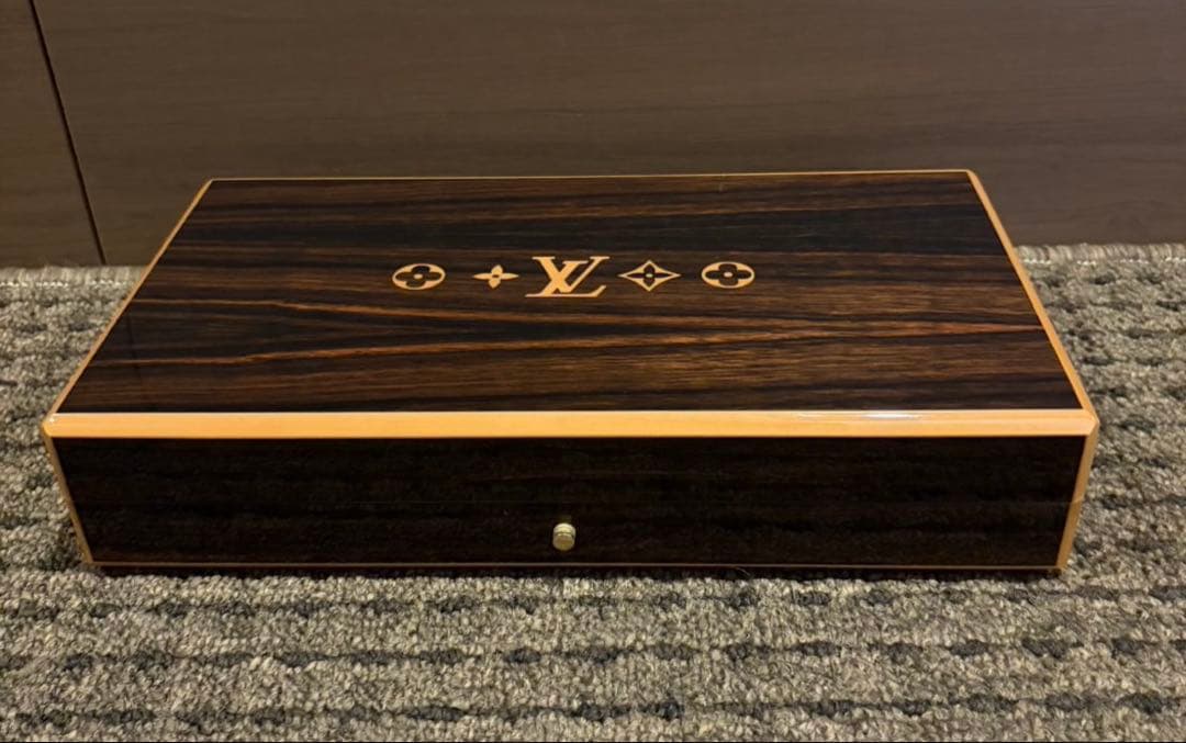 Closed wooden Louis Vuitton cigar case box (M58565) with LV monogram on the top, photographed on a carpeted floor.