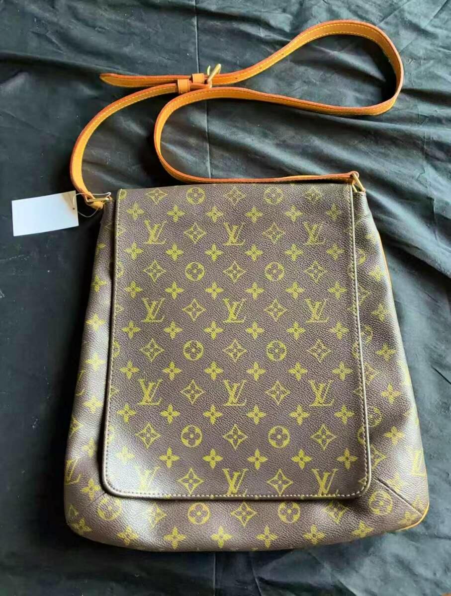 Front view of the Louis Vuitton bag (cow leather) showing the monogram pattern and a tan shoulder strap on a dark background.