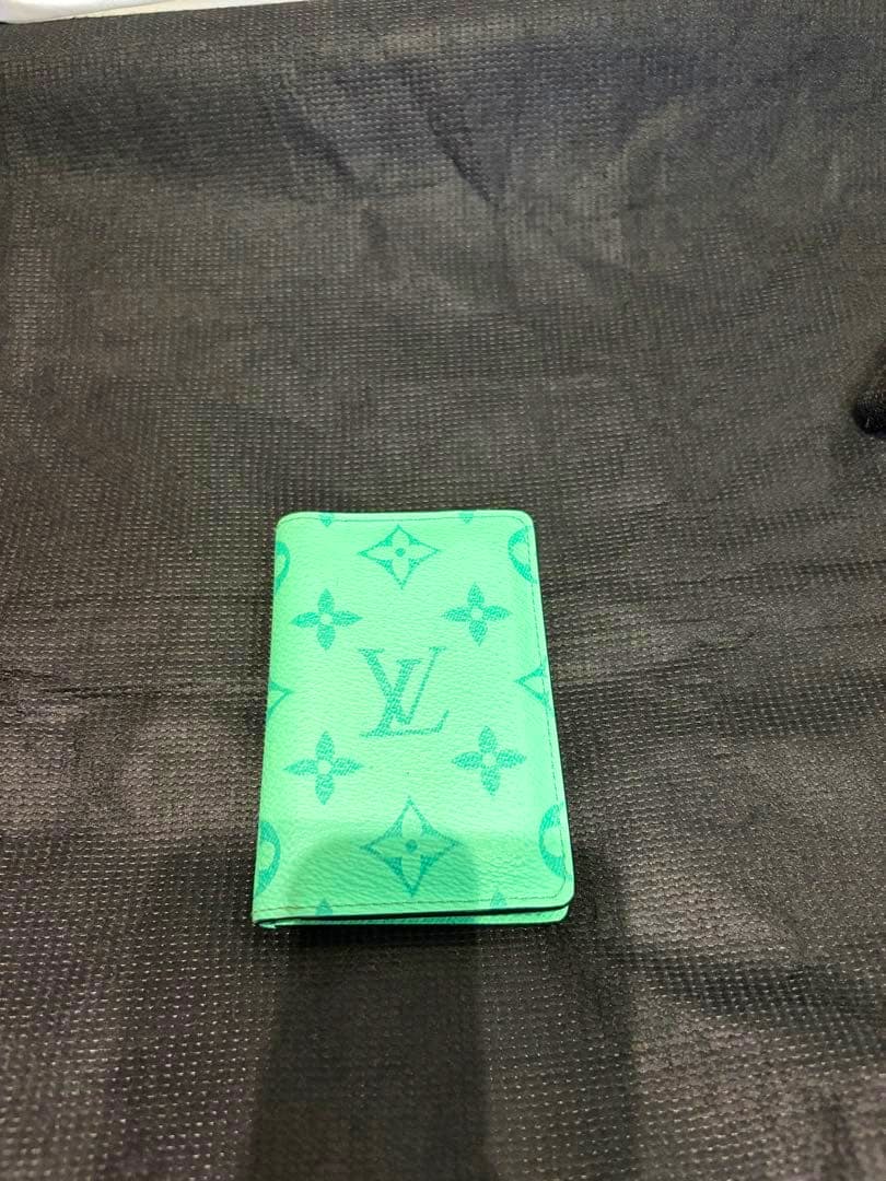 Mint green Louis Vuitton card case (cow leather) showing the monogram pattern placed on a black textured background.