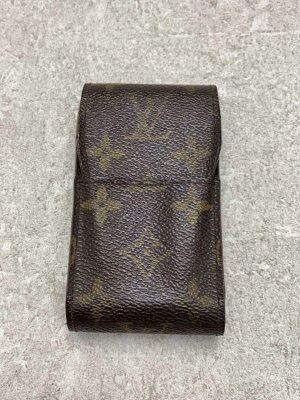 Brown Louis Vuitton monogram cigarette case in cow leather lying on a light textured surface.