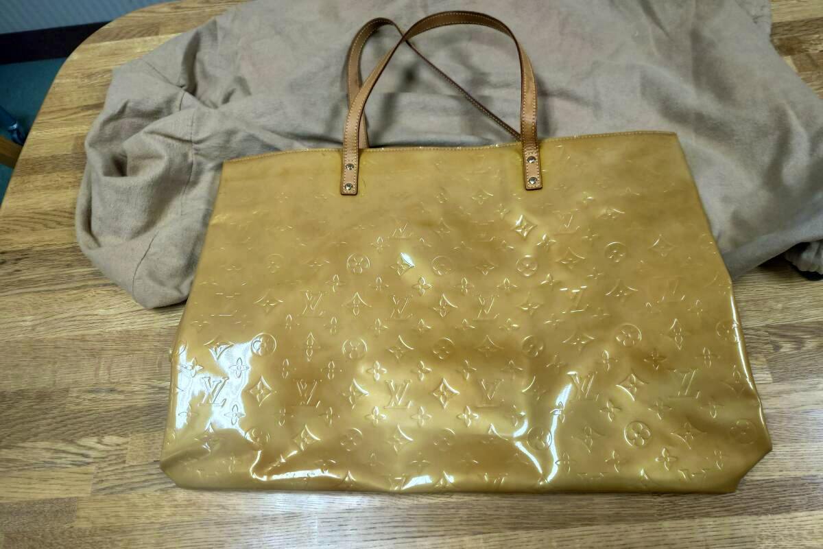 Patent leather Louis Vuitton shoulder bag with embossed monogram and two leather handles on a wooden surface.
