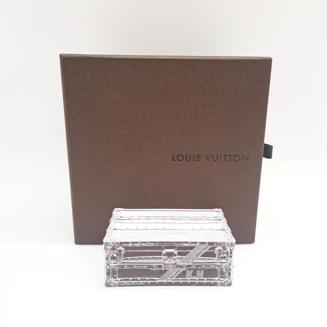 Clear crystal trunk-shaped paperweight displayed in front of a Louis Vuitton box.