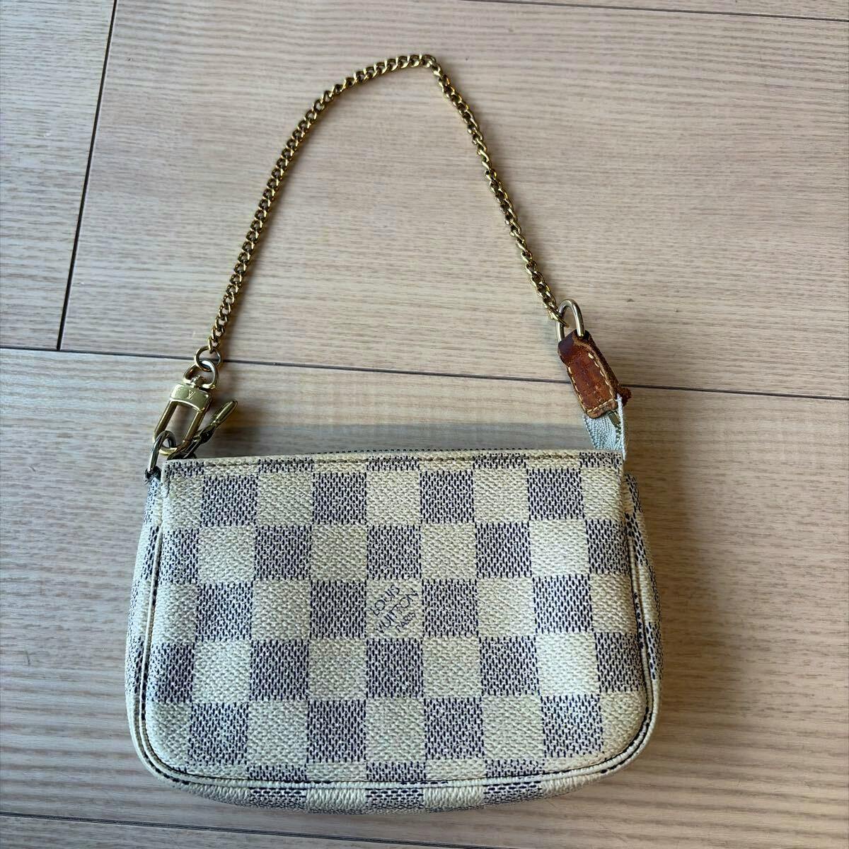 Louis Vuitton Damier Azur mini pochette accessoires canvas pouch with chain shown flat on a wooden floor.