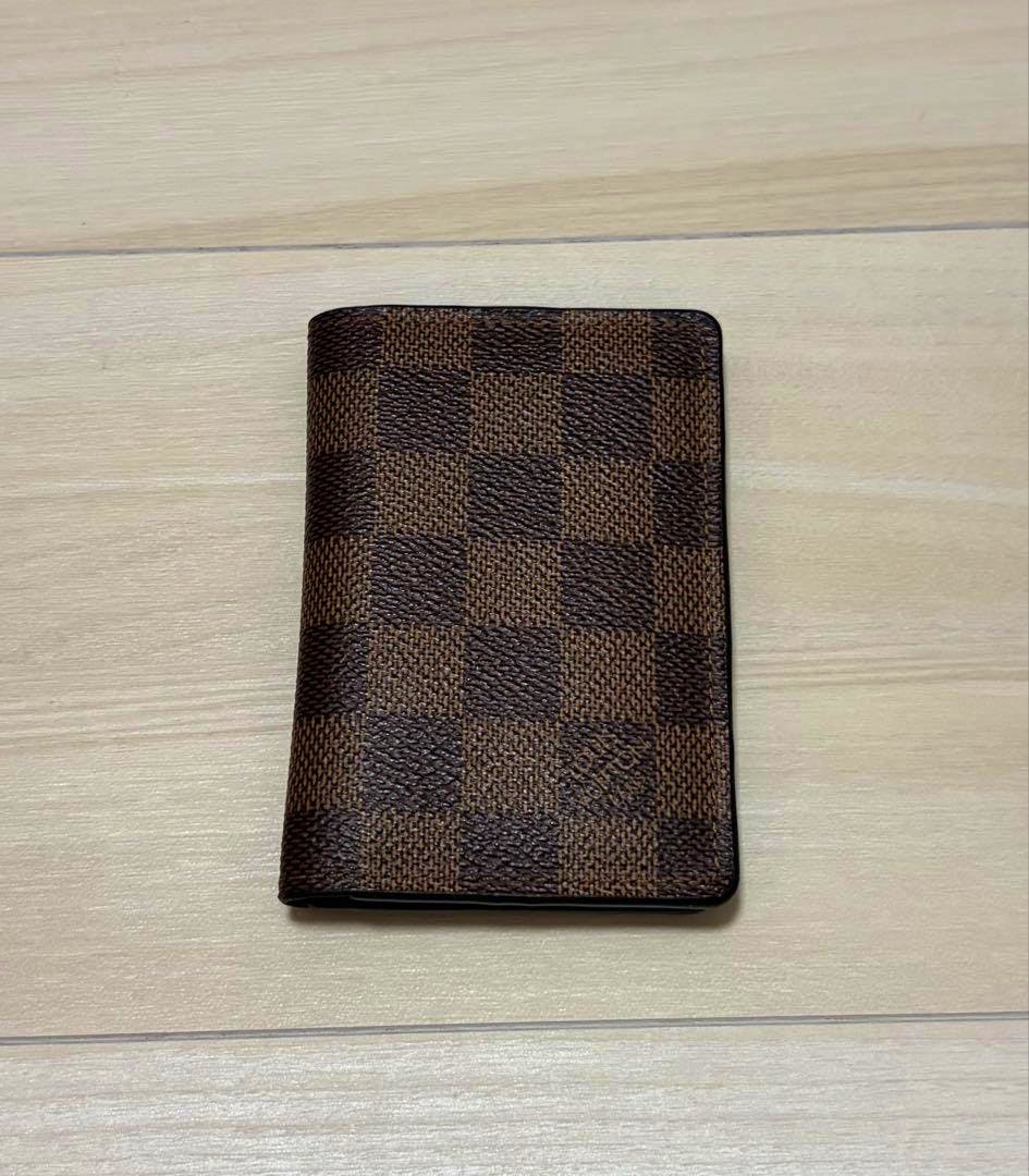 Closed Louis Vuitton Damier card case (wallet) placed on a light wood surface.