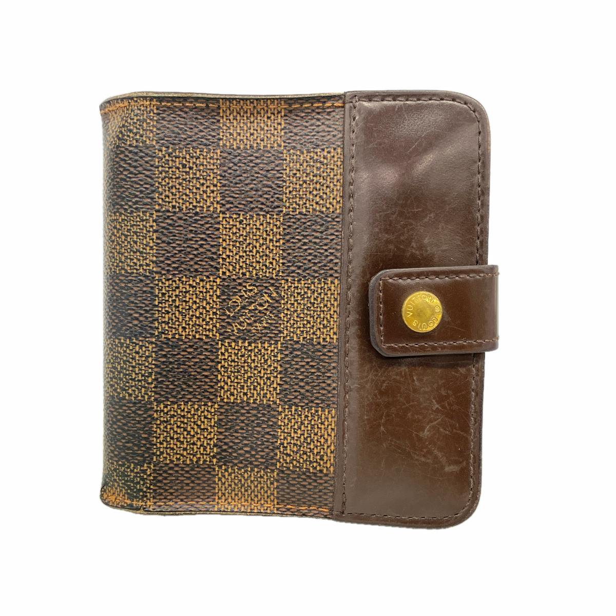 Closed Louis Vuitton Damier Ebene compact zip wallet with a brown leather snap tab on a white background.
