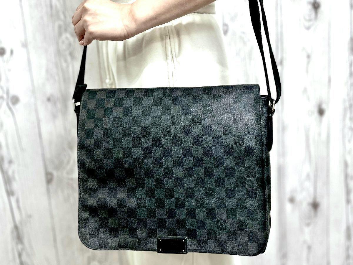 Front view of a black Louis Vuitton Damier Graphite District MM shoulder bag being held by a person.