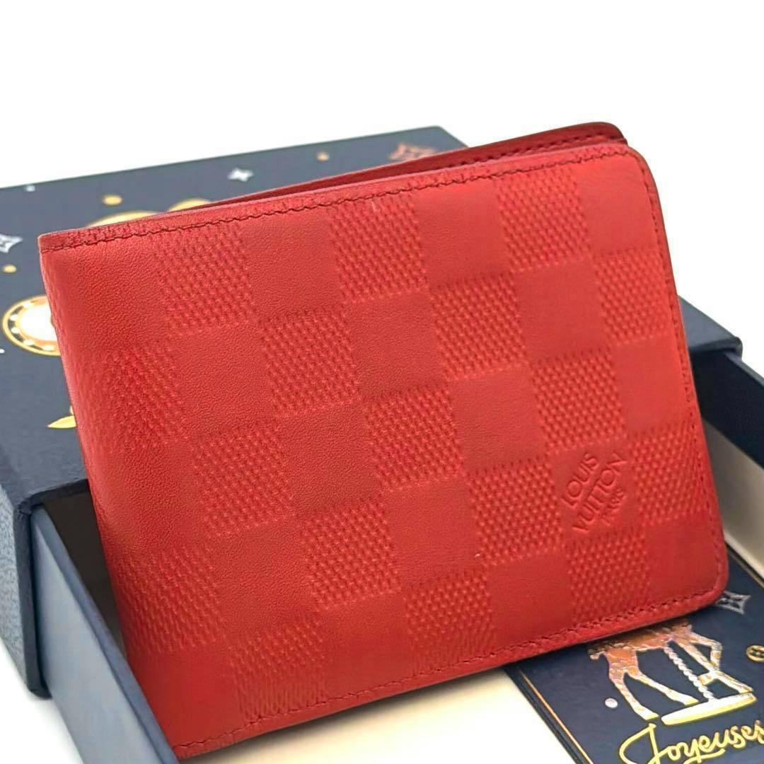 Orange Louis Vuitton two-fold wallet in Damier Anfini checkered pattern shown resting on a box.